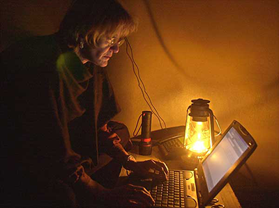 Photo of Kathy Gannon using a laptop by lantern light in a basement in Afghanistan