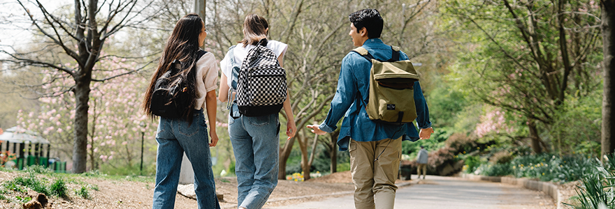 Three students with back packs walking on campus in the fall